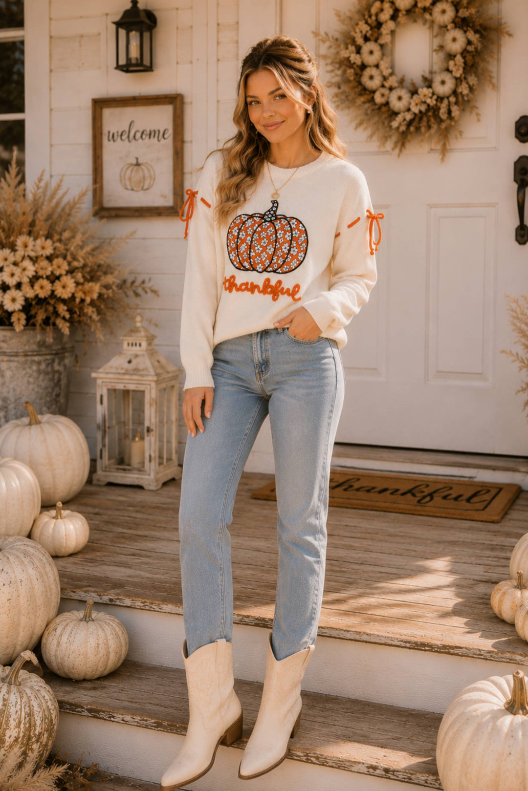 Woman wearing a sweater with a pumpkin design on a porch decorated for fall.