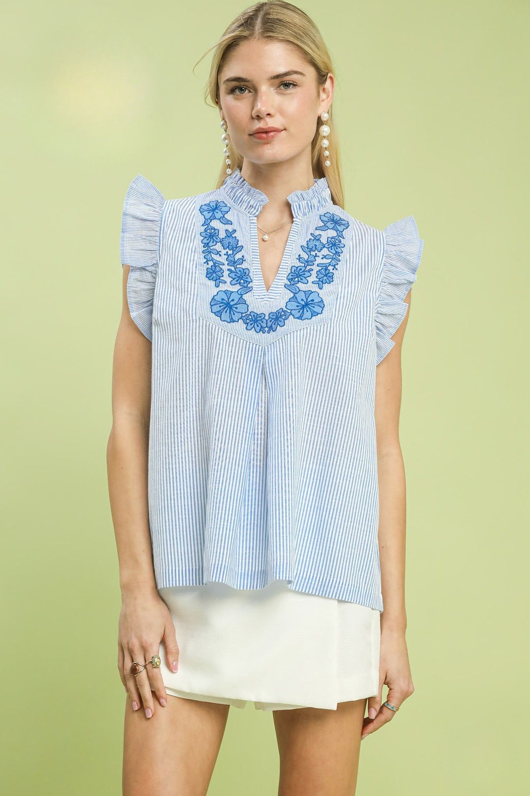 Woman wearing a blue and white striped blouse with floral embroidery on a light green background