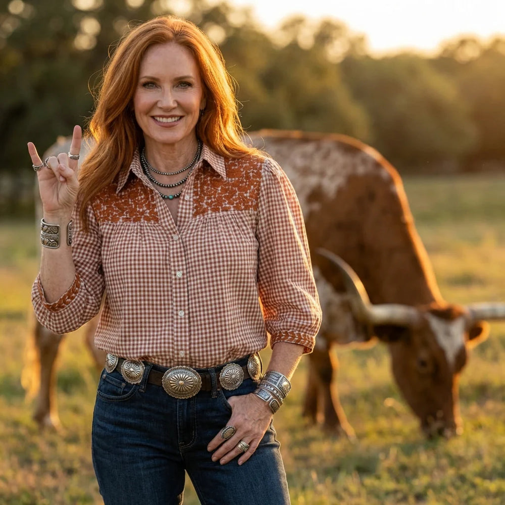 Woman in a plaid shirt and jeans standing in a field with a cow in the background