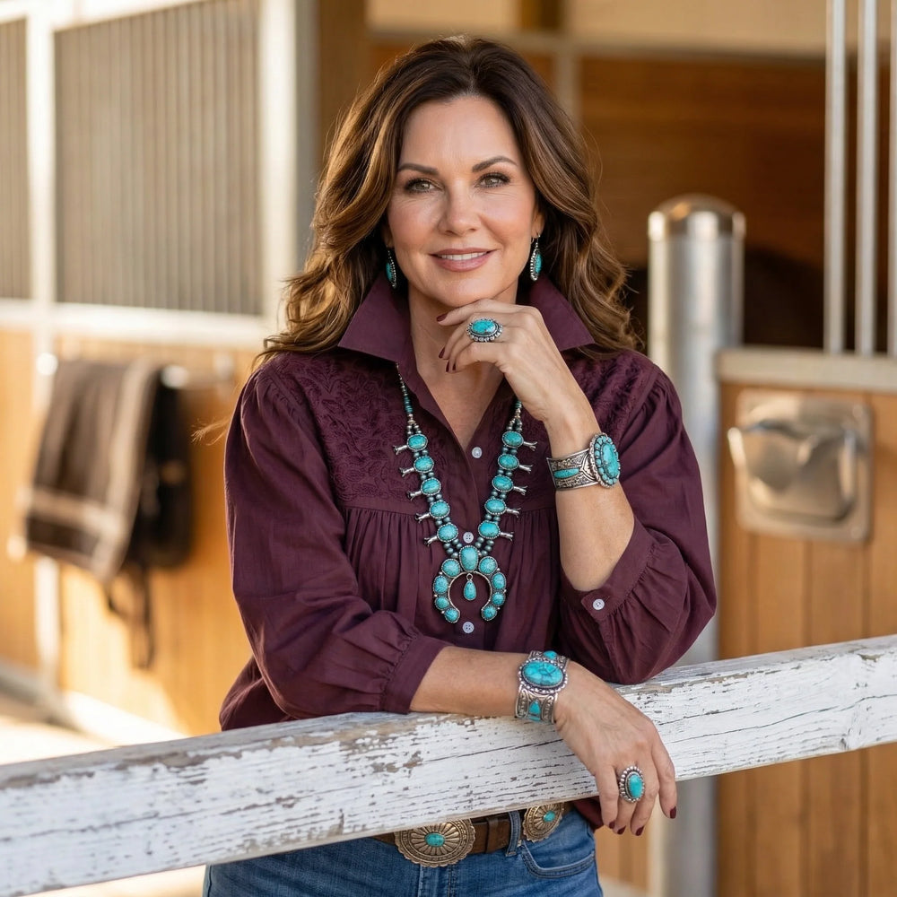 Woman wearing a purple shirt and turquoise jewelry leaning against a wooden railing.