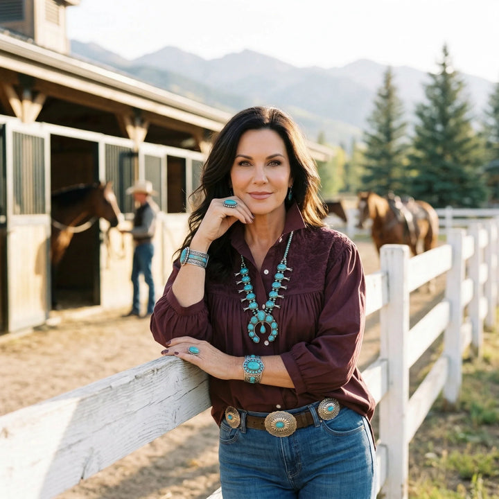 Woman standing in front of a stable with horses and mountains in the background