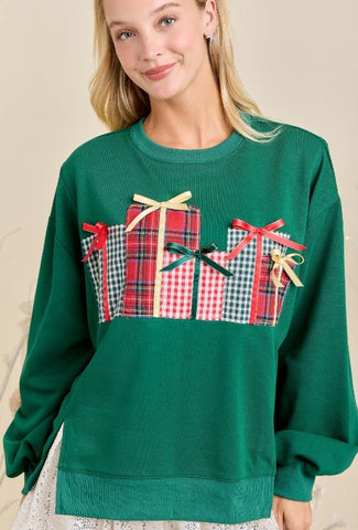 Green sweater with plaid gift box design worn by a model against a beige background